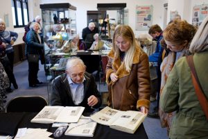 An older man and a younger woman looking at scrapbooks at the Shoemaking in Cockermouth exhibition
